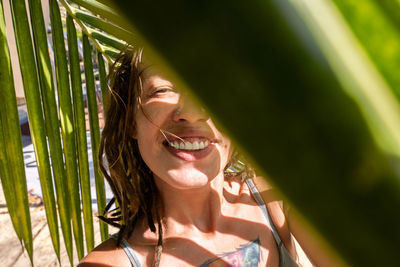 Smiling woman taking selfie under palm leaf on tropical beach. summery vacations moment.