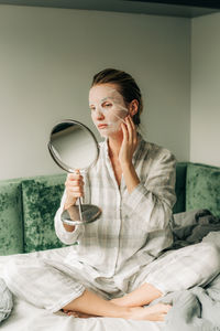 Woman applying textile facial moisturizing mask, beauty and skin care concept.
