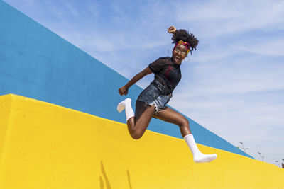 Low angle view of woman shouting while jumping against sky