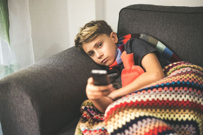 Boy resting on sofa with blanket while watching television at home