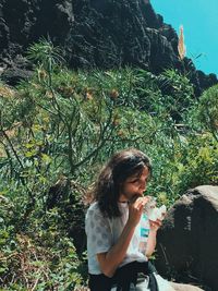 Female hiker eating food while sitting on rock during sunny day