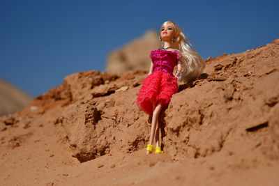 Pink doll on sand against clear blue sky