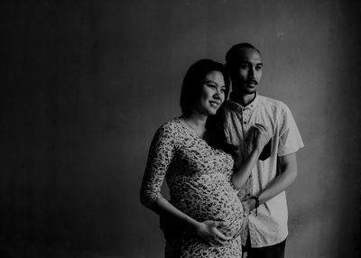 Man with pregnant wife standing against wall