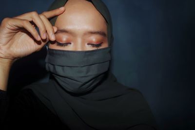 Close-up of woman wearing mask against black background