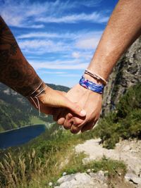 Close-up of couple holding hands against sky