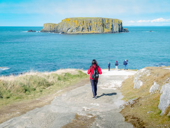 Man standing on rock by sea against sky