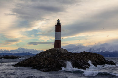 Lighthouse by sea against sky during sunset