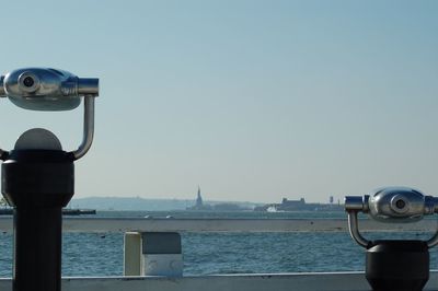 Coin-operated binoculars by sea against clear sky