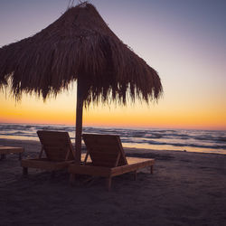 Chair on beach against sky during sunset
