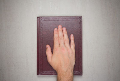 Close-up of hand on open book against wall