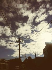 Low angle view of electricity pylon against cloudy sky