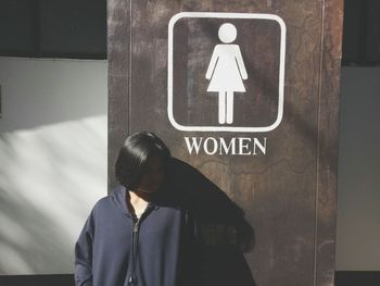 Teenage girl standing against female restroom sign