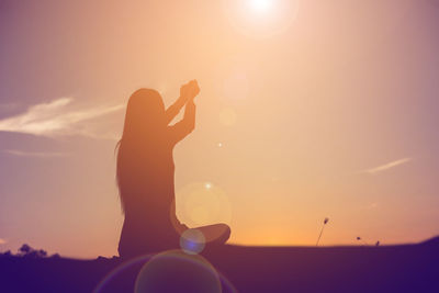 Silhouette woman holding sun against sky during sunset