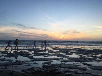 Silhouette people on beach against sky during sunset