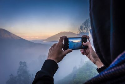 Midsection of man using mobile phone against mountains