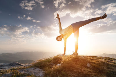 Woman practicing yoga in a pose stands on a rug on stones in the mountains against the background of