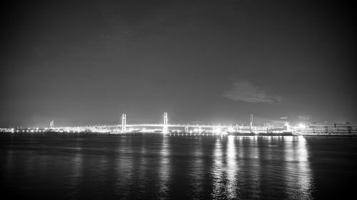 Illuminated city by sea against sky at night