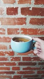 Cropped hand holding tea against brick wall