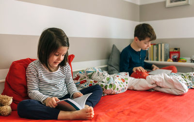 Siblings reading books on bed at home