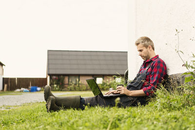 Man using laptop while sitting on grassy field at farm