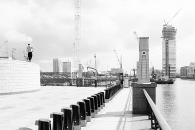 Rear view of man overlooking cranes and buildings by river