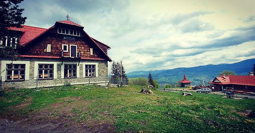 House on field by buildings against sky