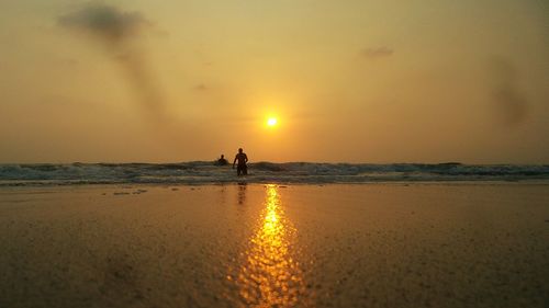 Silhouette people at beach against sky during sunset