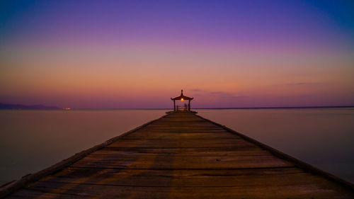 Gazebo on pier over sea against orange sky