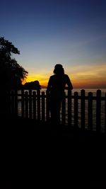 Silhouette man standing by sea against clear sky during sunset