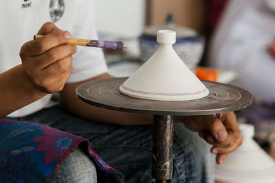 Midsection of craftsperson painting earthenware on spinning wheel at workshop