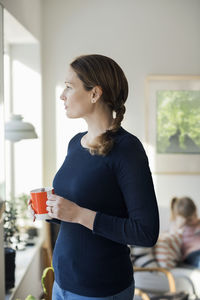 Woman standing with coffee cup in living room at home