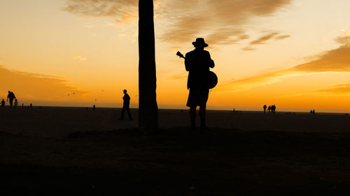 Silhouette man playing music at beach against sky during sunset