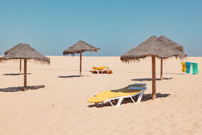 Lounge chairs and parasols on beach against clear sky