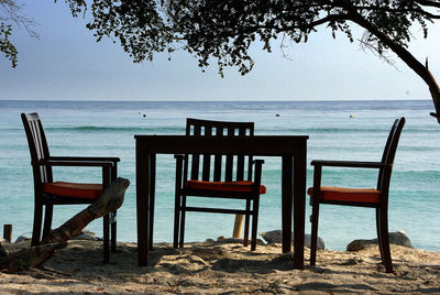 Chairs and table on beach against clear sky