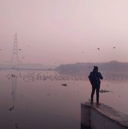 Man standing on river against sky during sunrise