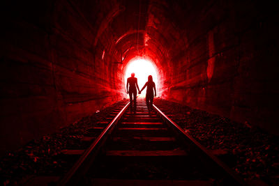 Silhouette man and woman standing on railroad track in tunnel