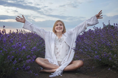 Young woman with arms raised on purple flowering plants