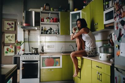 Side view of woman drinking coffee while sitting at kitchen 