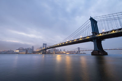 Illuminated bridge over river against sky at night