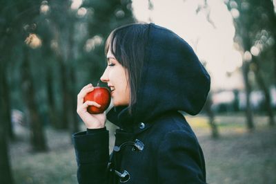 Smiling young woman holding red apple while standing at park