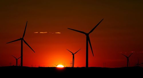 Silhouette windmills against sky during sunset