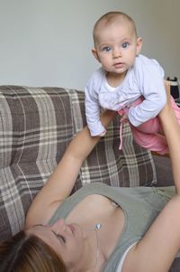 Low angle view of mother playing with baby while lying on sofa at home