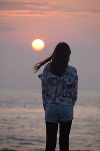 Rear view of woman standing against sea during sunset