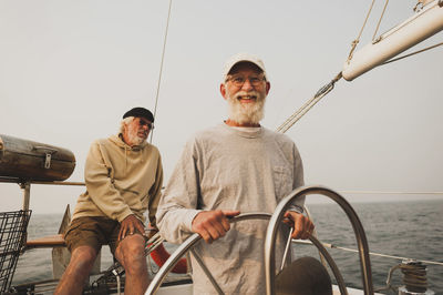 Portrait of senior man with friend sailing boat on sea against clear sky