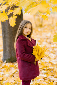 Cute six year old girl in burgundy clothes and a beret walks through the autumn park at sunset