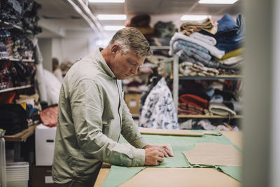 Side view of mature fashion designer marking on fabric while working at workshop