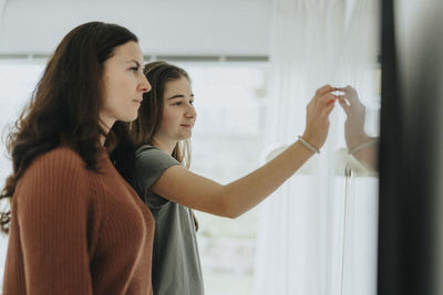 Daughter touching smart tv mounted on wall by mother in living room