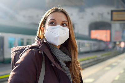 Portrait of casual woman waiting train with kn95 ffp2 protective mask at train station on winter