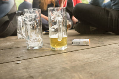Friends sitting by beer glass and cigarette pack on boardwalk