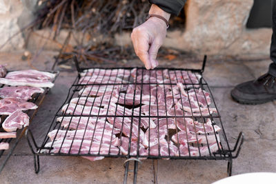 Unrecognizable man is adding salt to the raw meat in the grill before cooking in the barbecue.